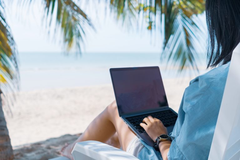 Woman working on a laptop on the beach under palm trees